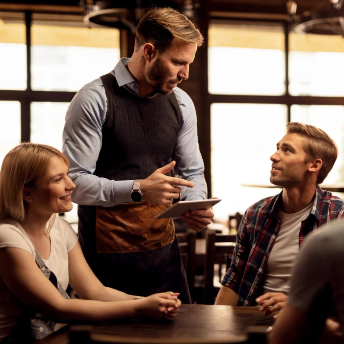 Garçom a atender uma mesa de amigos num pub com tablet na mão