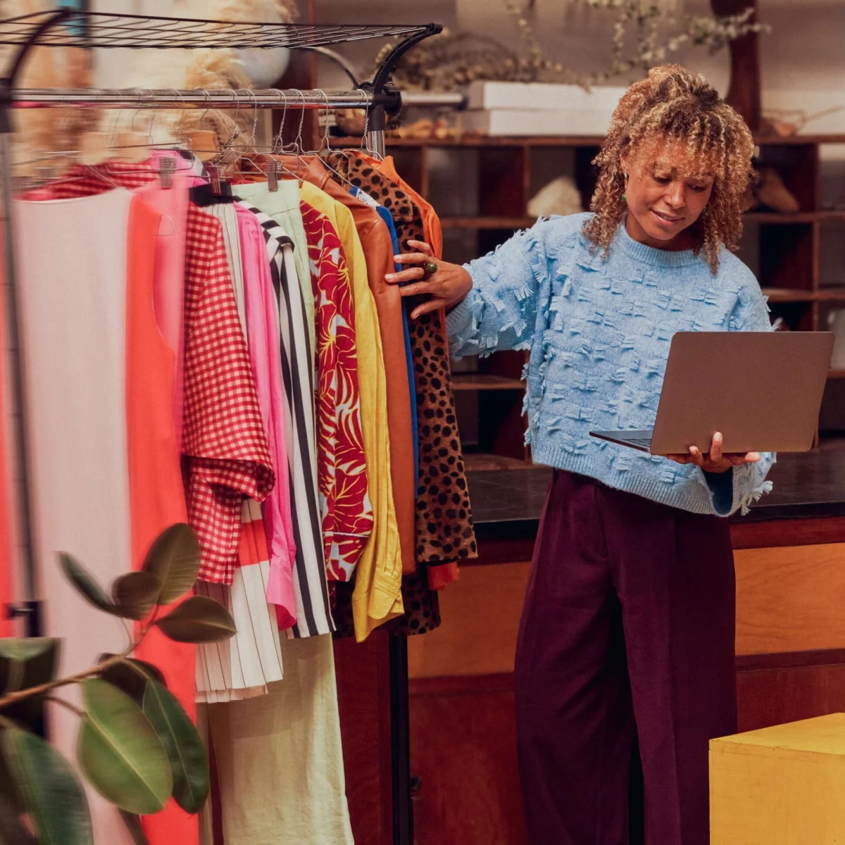 Mulher a analisar roupas em loja com portátil na mão